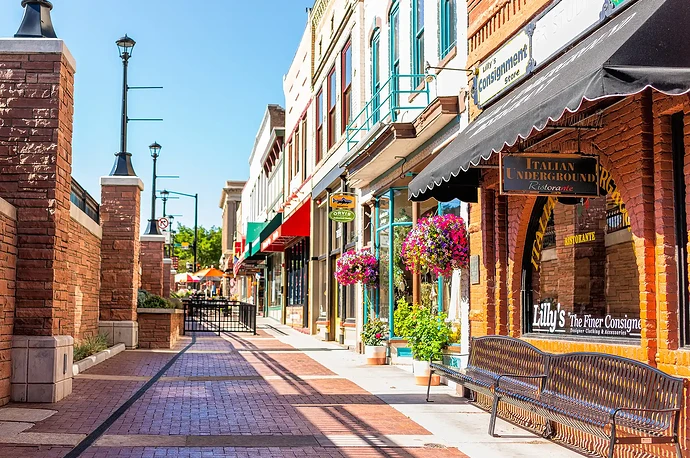 A town street with brick pavement storefronts benches and hanging flower baskets