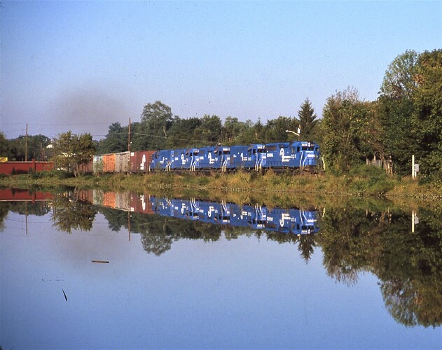 An eastbound freight led by GP40 #3220 passes the Agway store at the New Market Pond, Piscataway, NJ. September 1981.